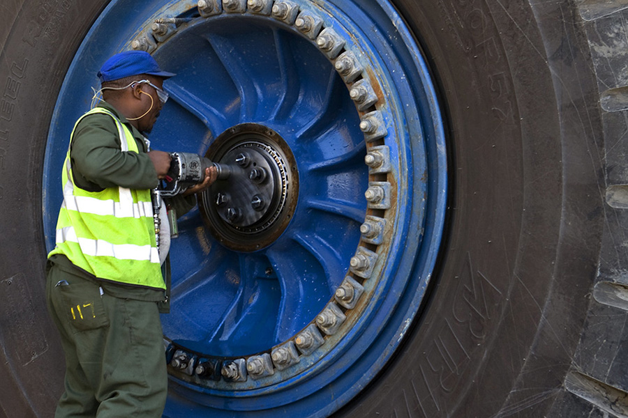 A man uses a tool to secure bolts into a wheel much bigger than himself.