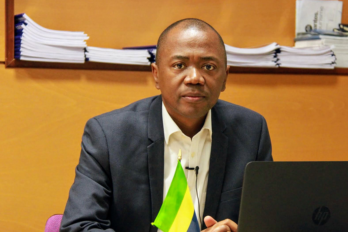 Portrait of a man in front of a laptop and a flag. 