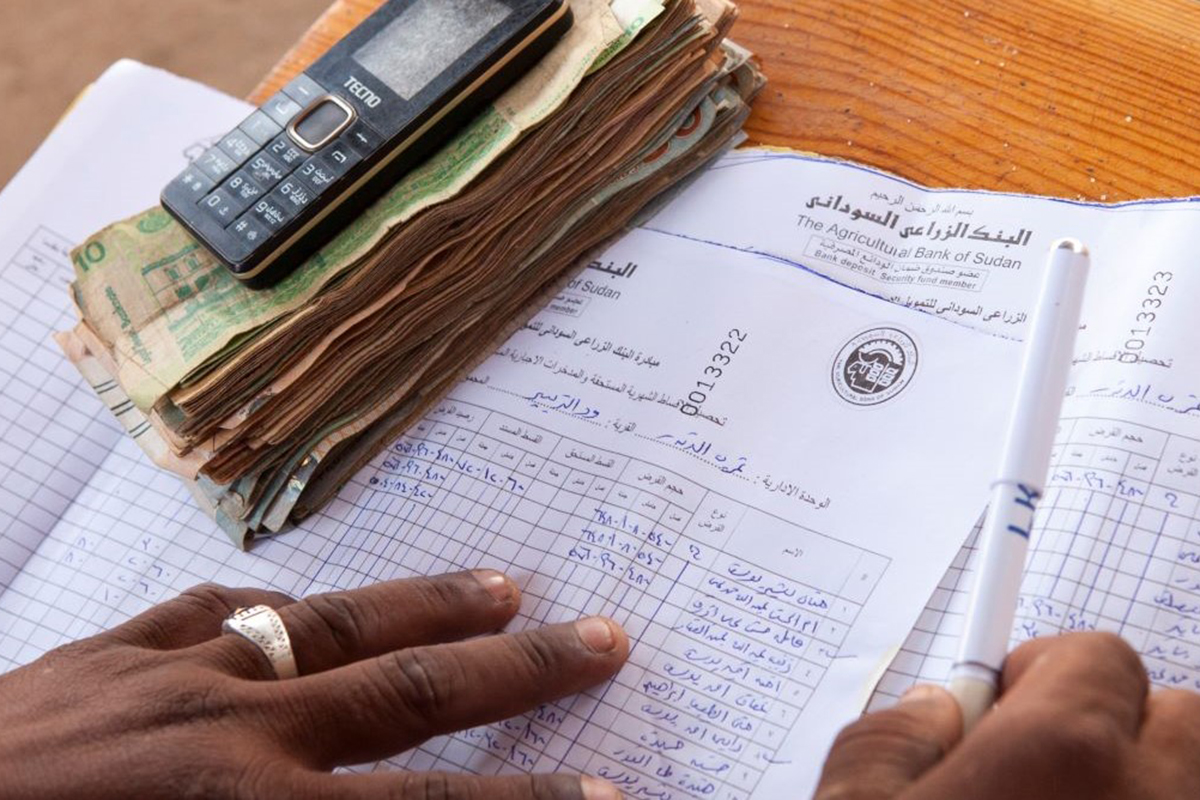 Hands on a paper spreadsheet with currency and a calculator near by.