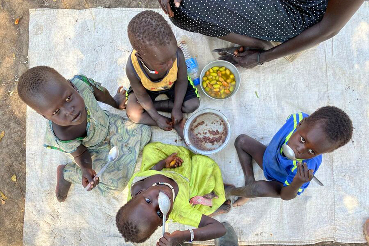 Four children eating on the ground look up at the camera.