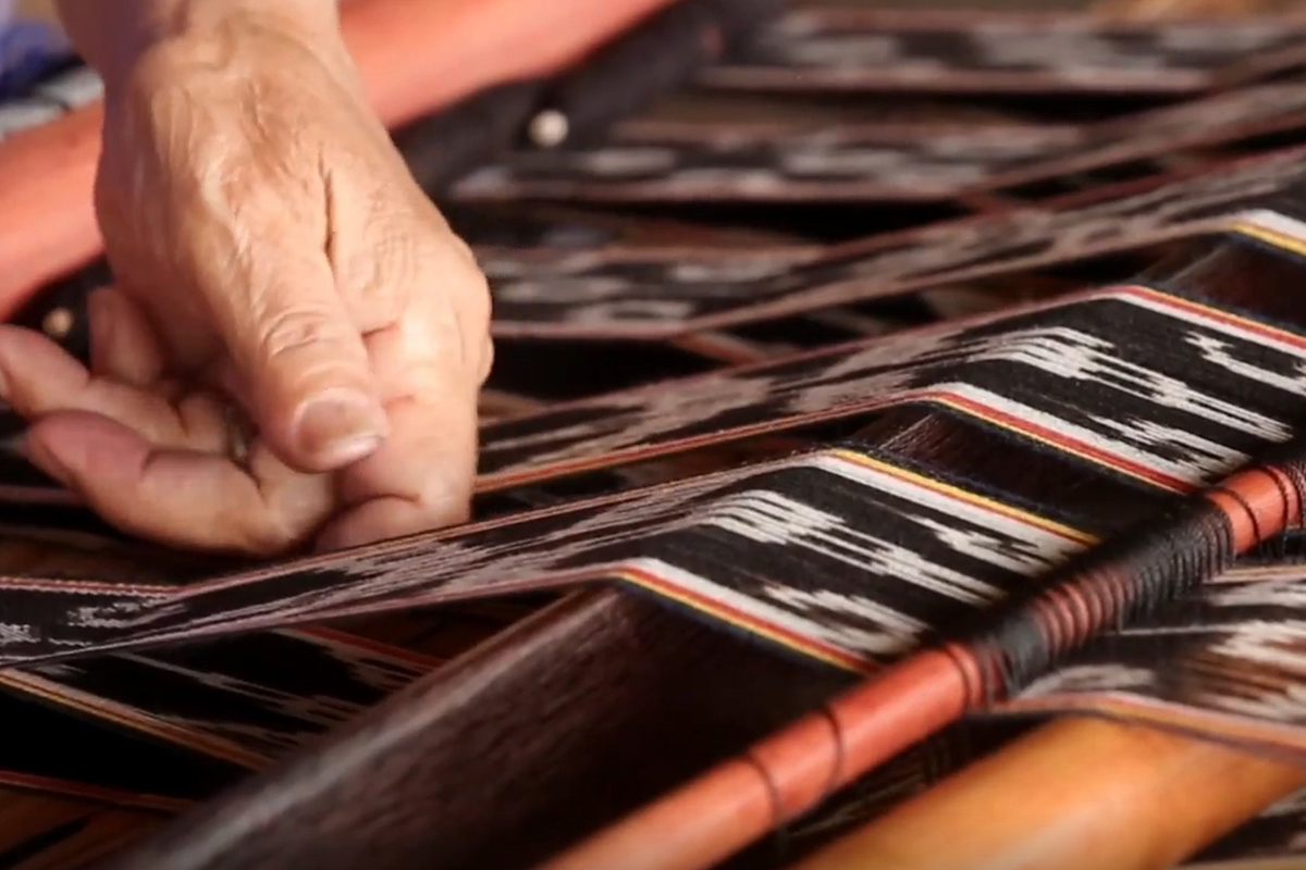 A hand smooths a textile on a hand loom