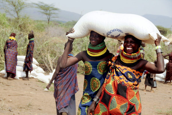 Two women together carry one bag of aid on their heads. 