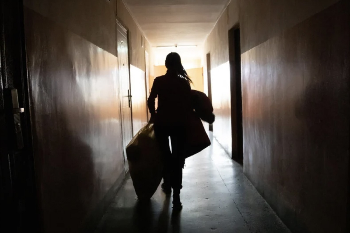 A woman carrying loads in a dark corridor