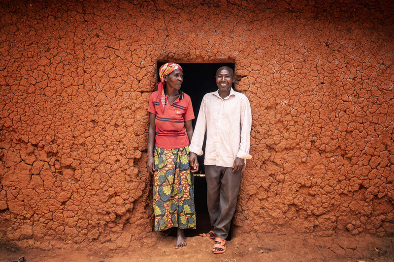 A couple holds hands in front of the doorway through mud walls