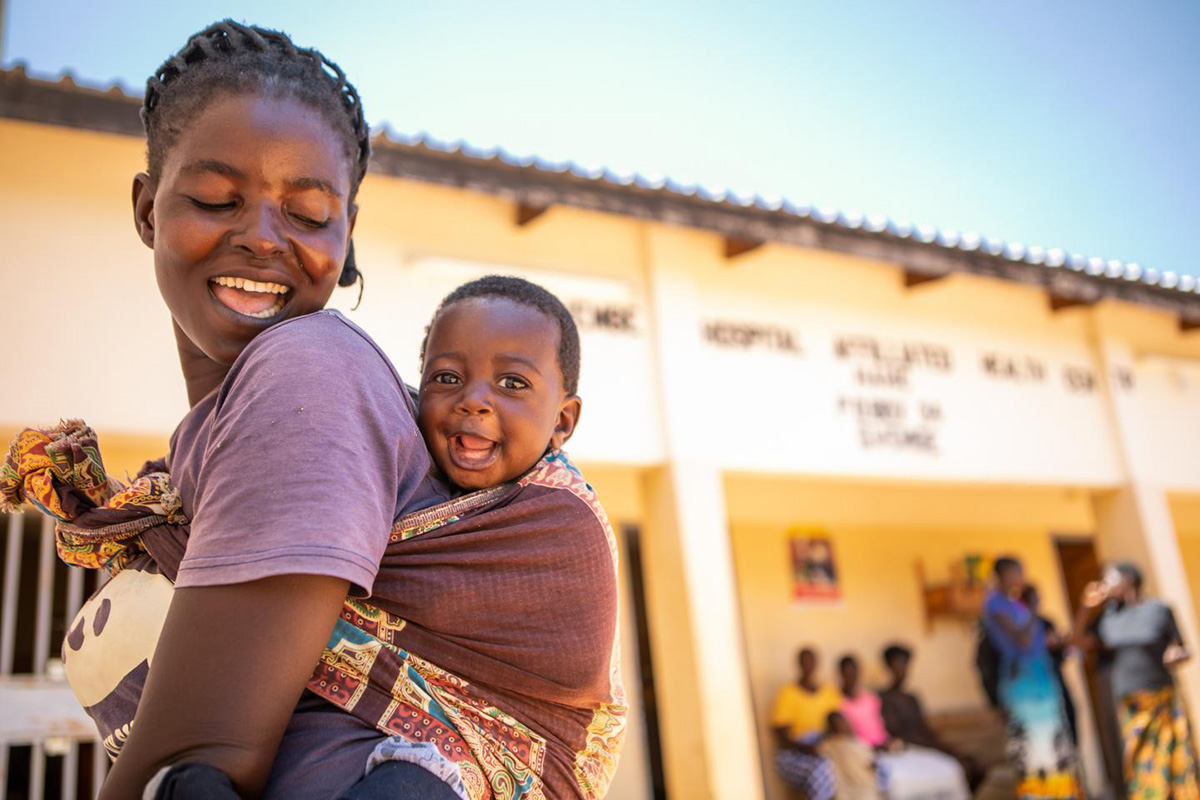 A smiling mother carries her smiling baby on her back