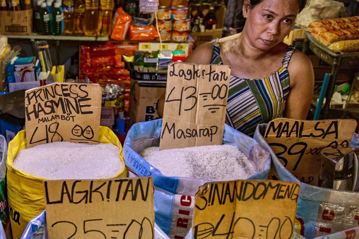 A woman behind sacks of food with price signs in a market stall