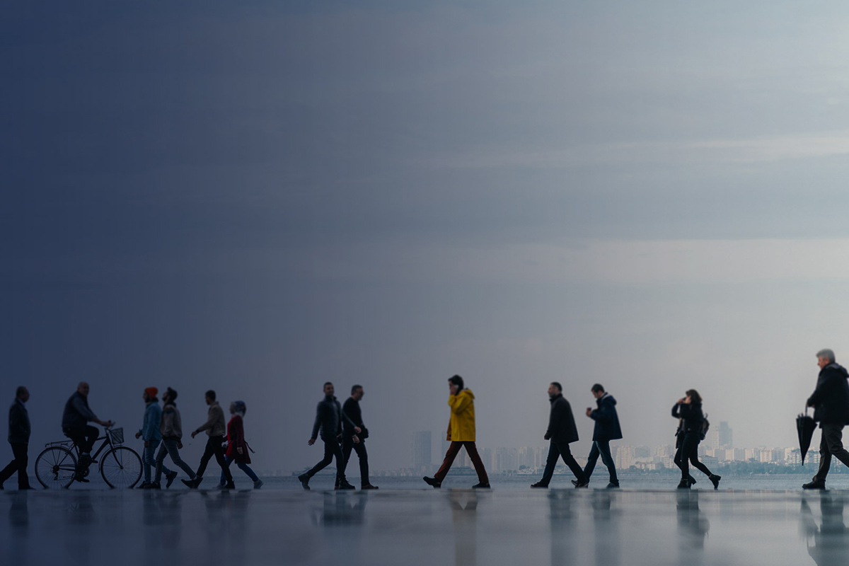 A city scape with people walking by as the light dims from one end the other. 