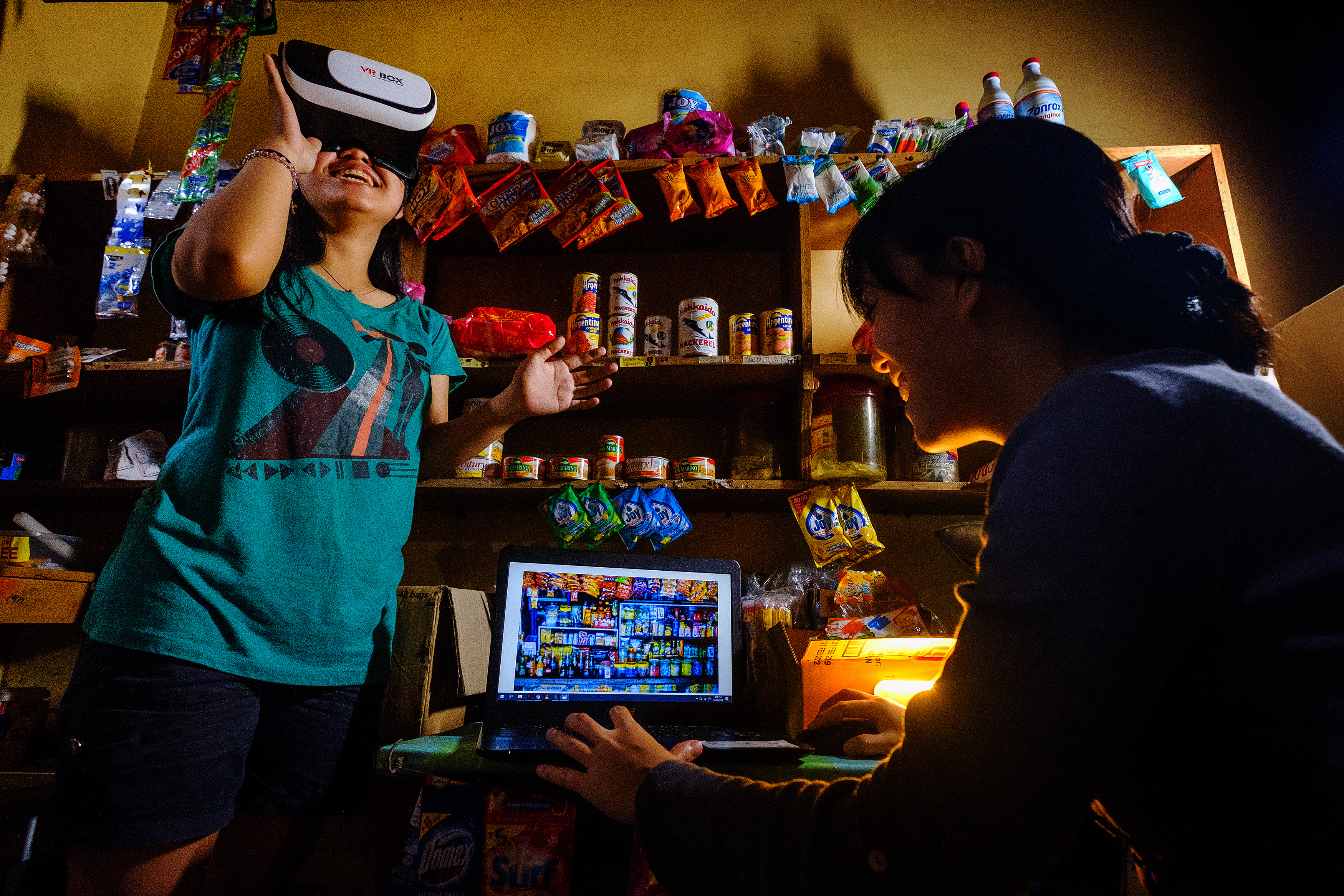 two girls using virtual reality goggles and a laptop inside a pantry with low light