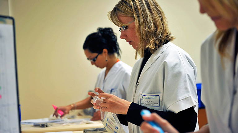 Three women in white coats standing in front of table and working.