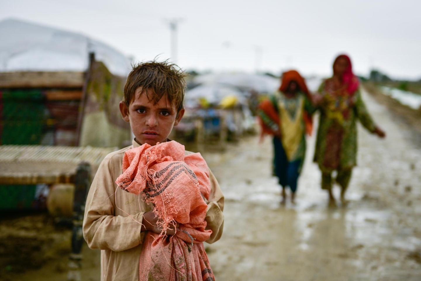 Boy standing in mud holding pink bag.