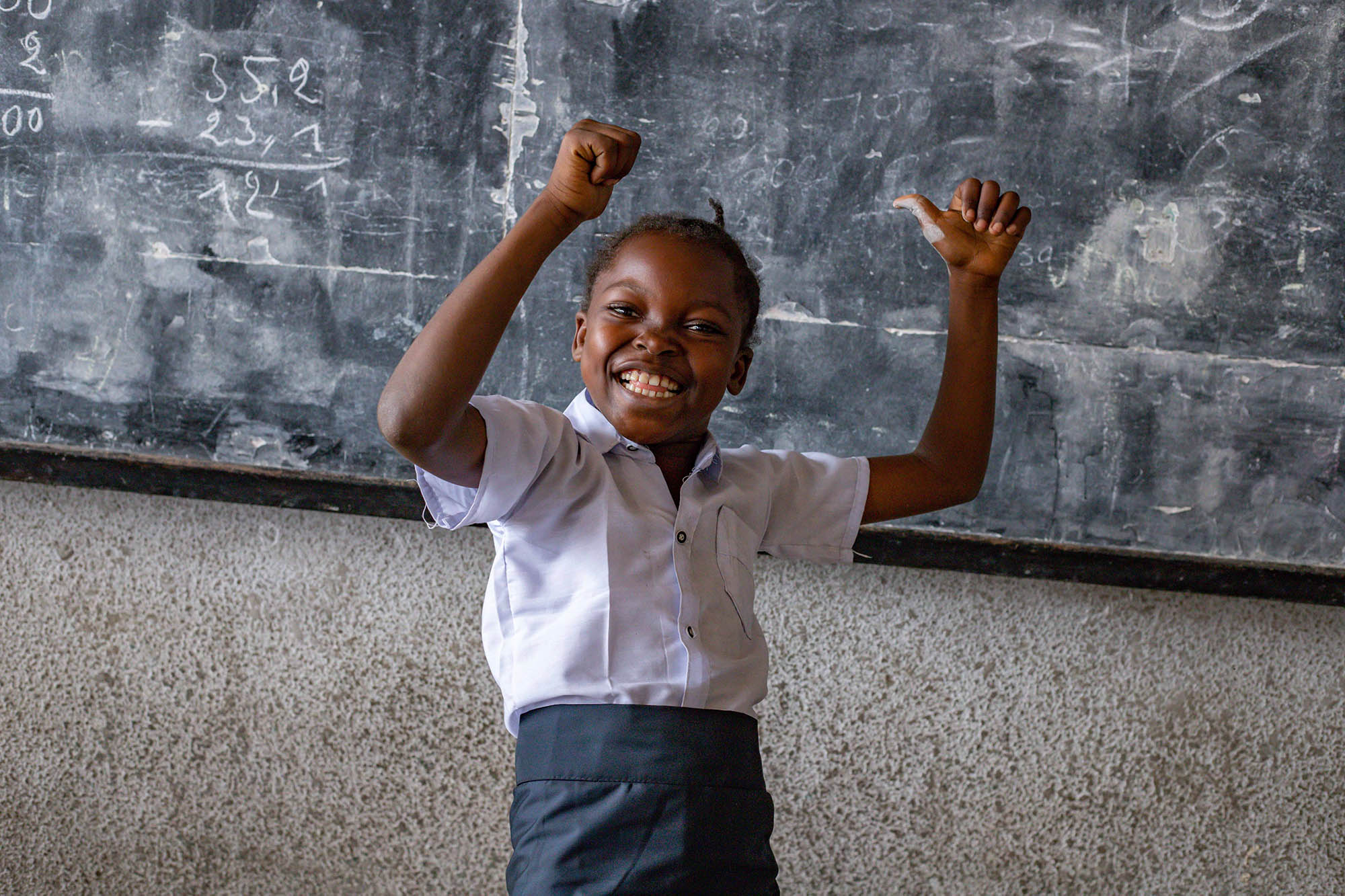 schoolgirl showing thumbs up in front of blackboard