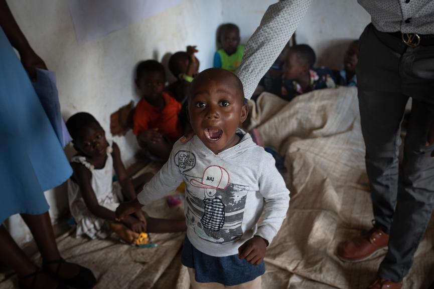 Boy standing with adult surrounded by children at vaccination centre