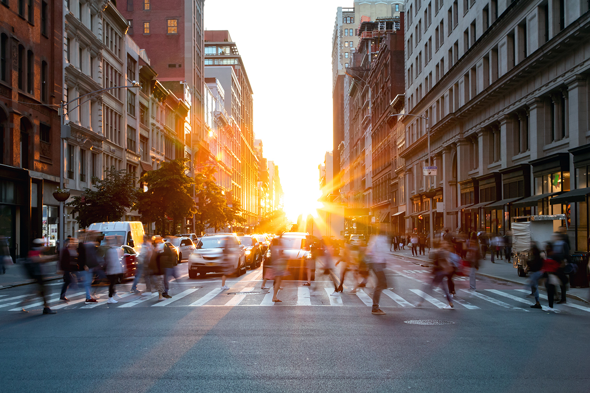 people crossing the street at a cross walk as cars wait