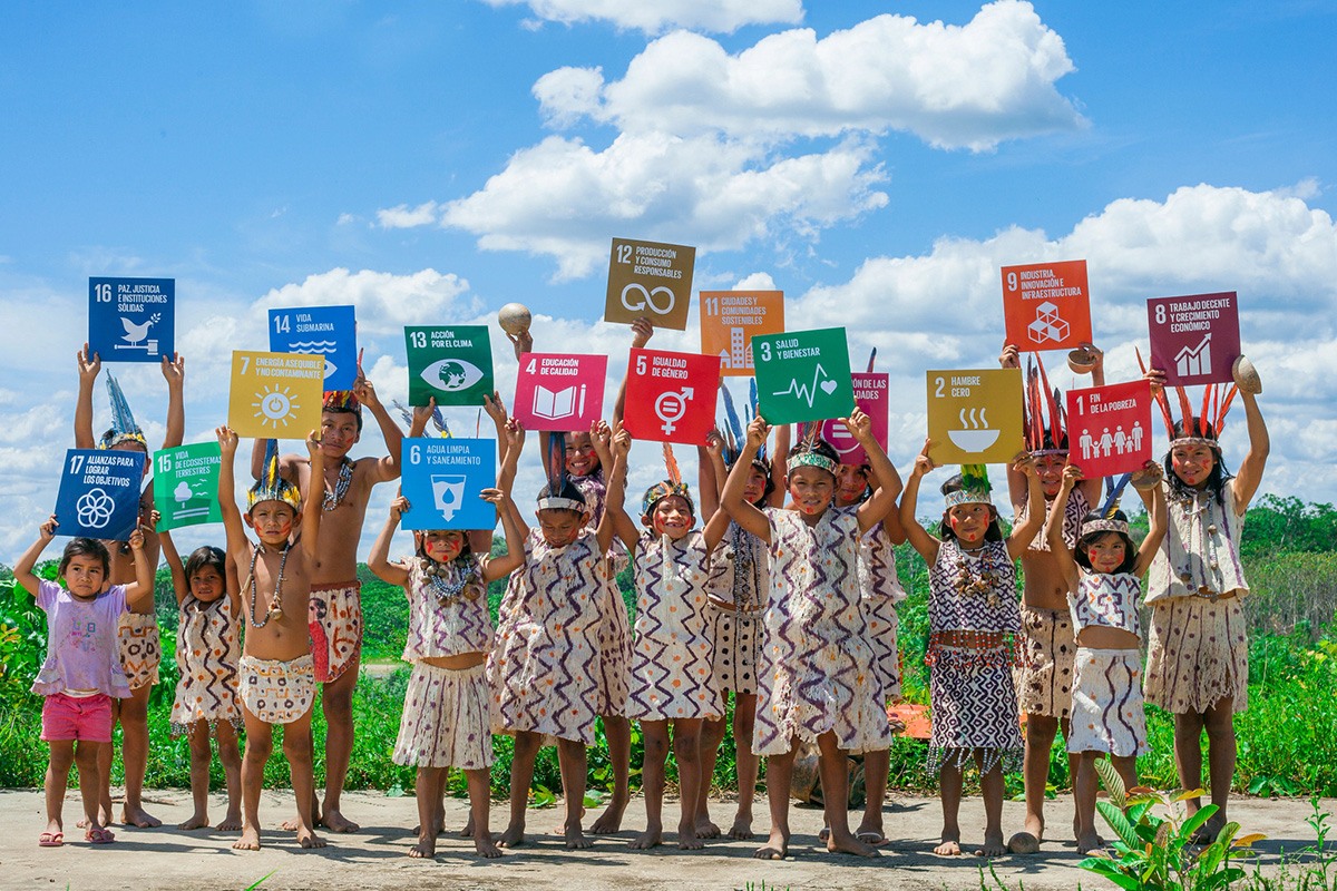 Children from the Amazon dressed in traditional outfits hold up signs of the individual SDGs.