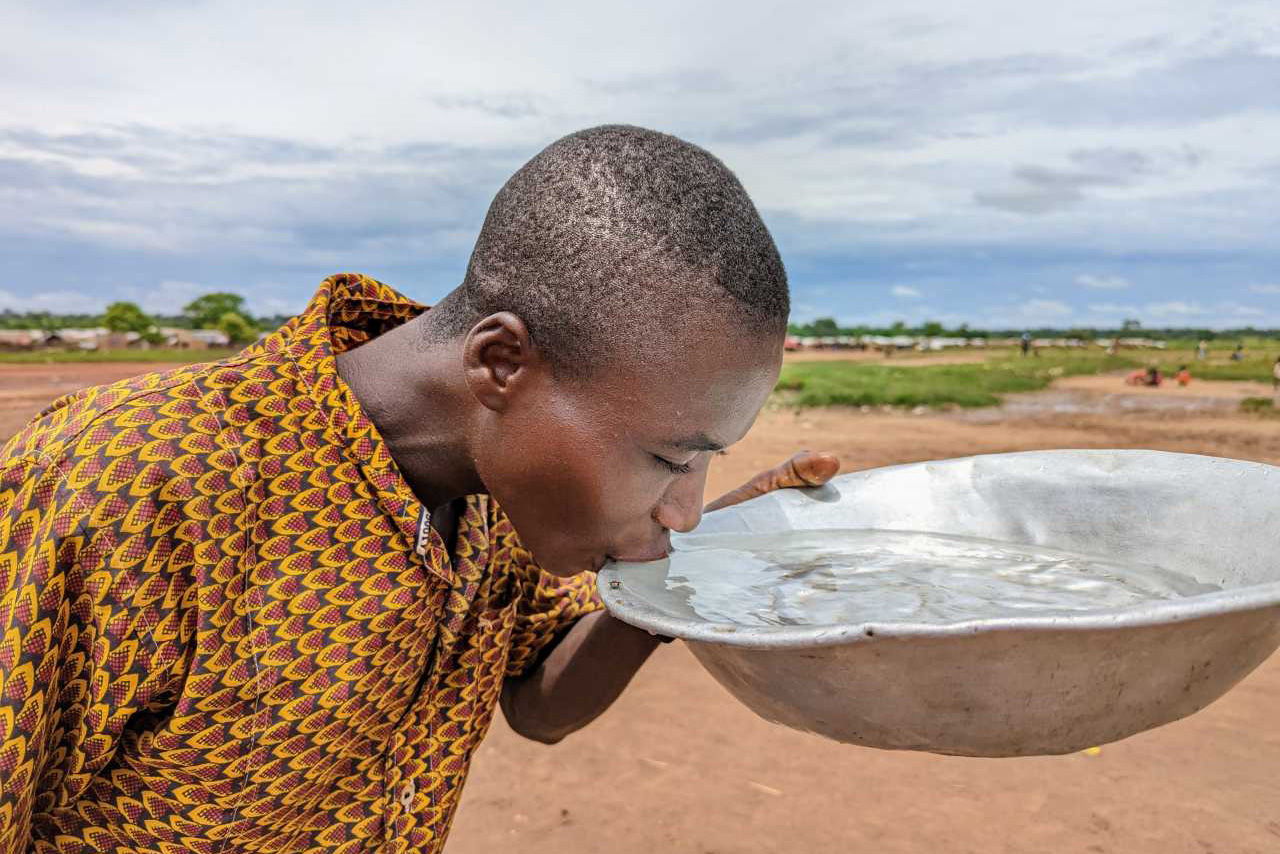 A man takes a sip of water from a large metal bowl.