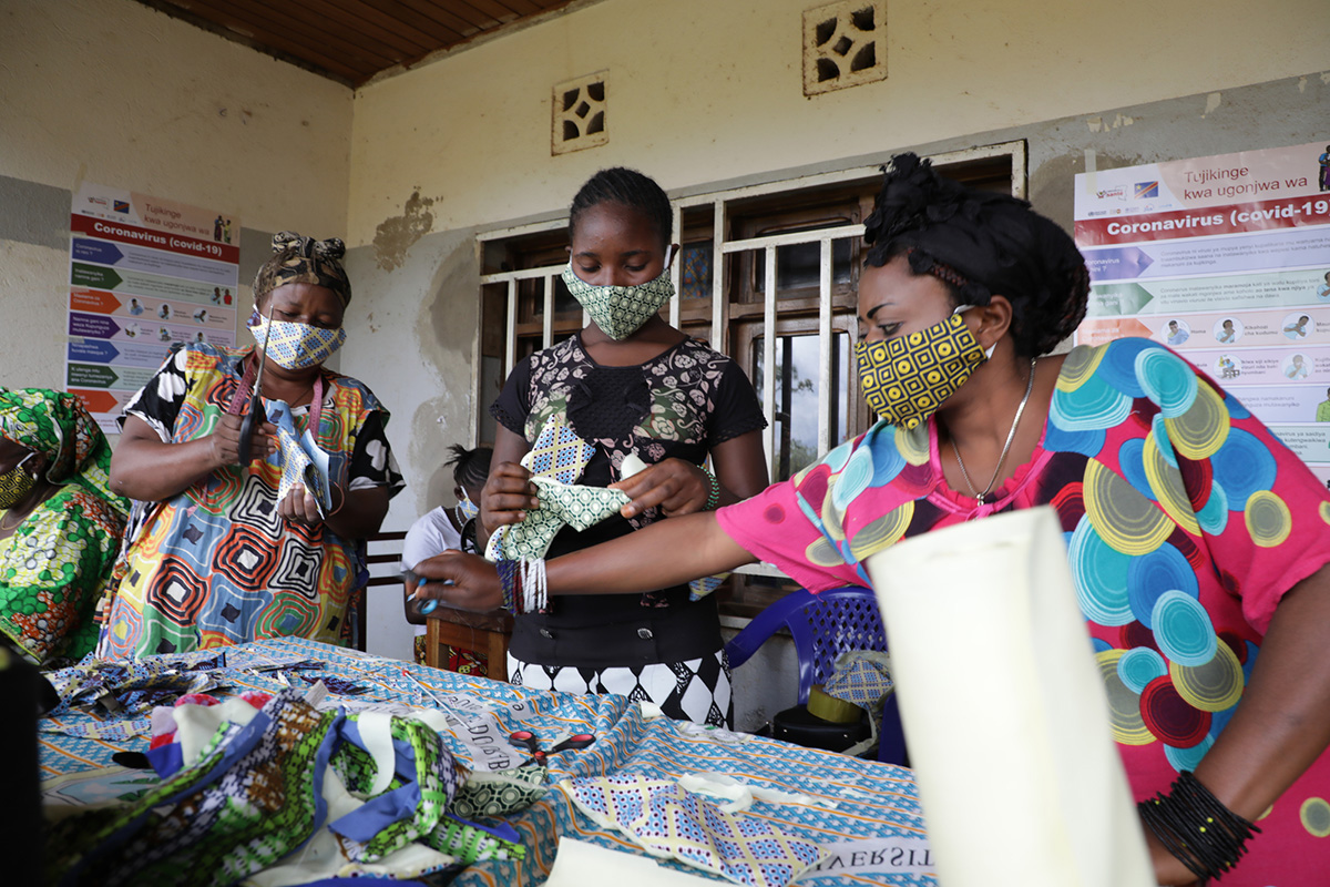 three ladies stand in front of a table with fabrics of African patterns