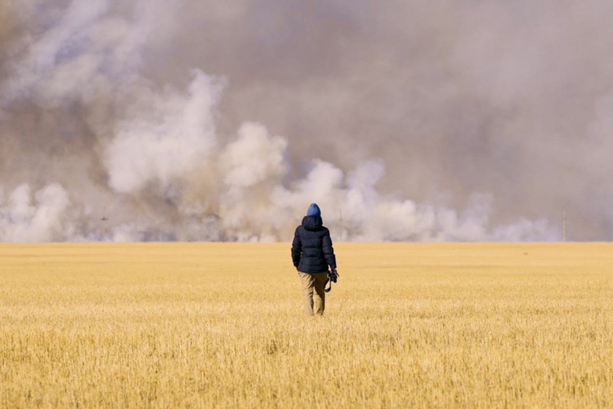 a man stands in the middle of a grass field with smoke in the background