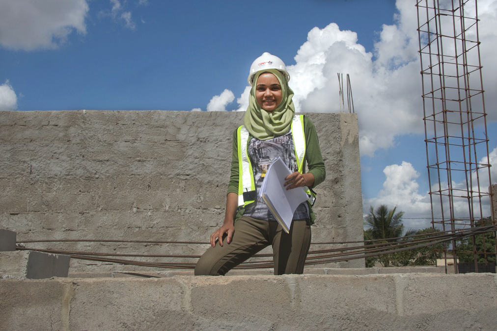 A woman wears a headscarf, a helmet and a safety vest from a construction site.