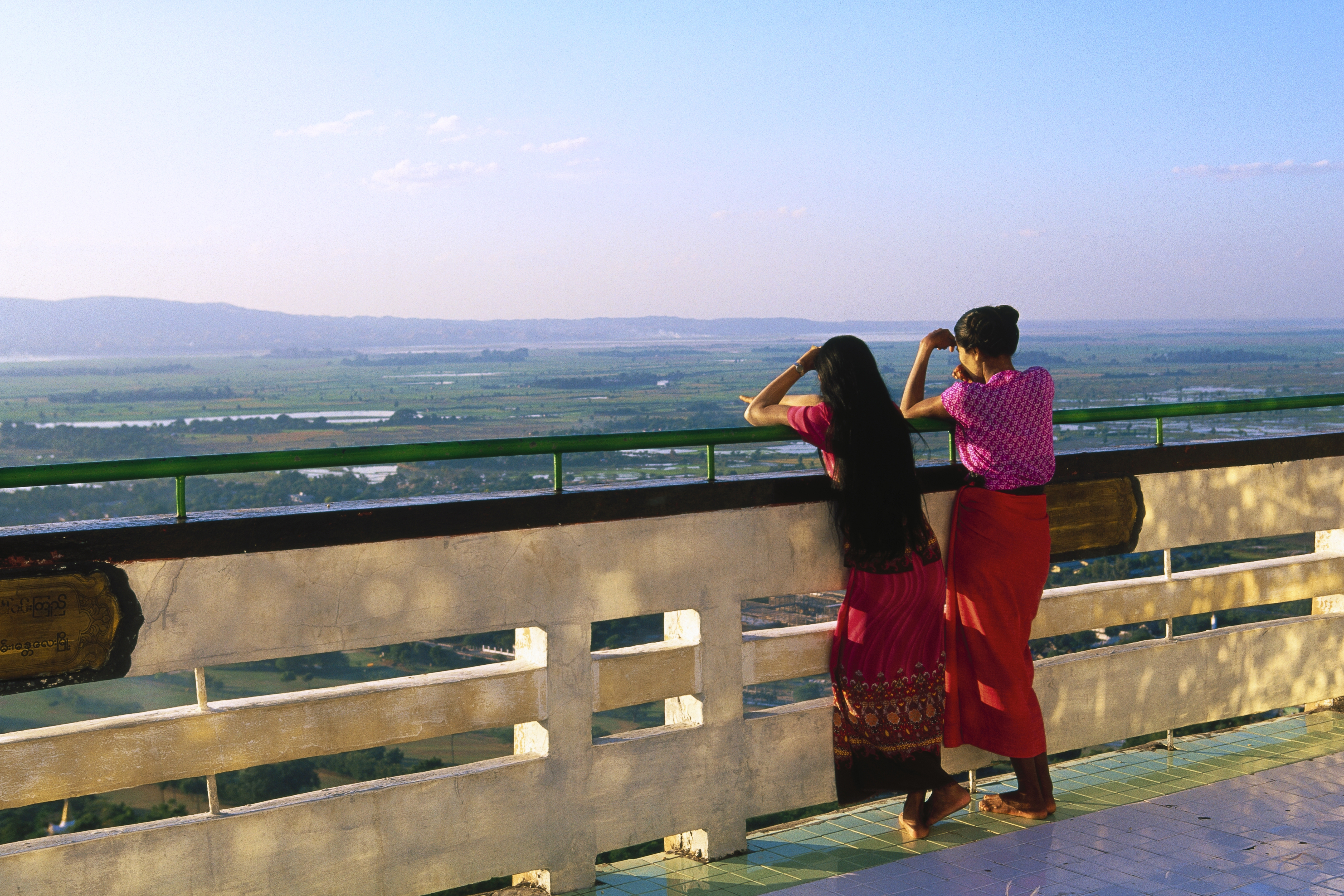Two girls look out at the horizon from a bridge.