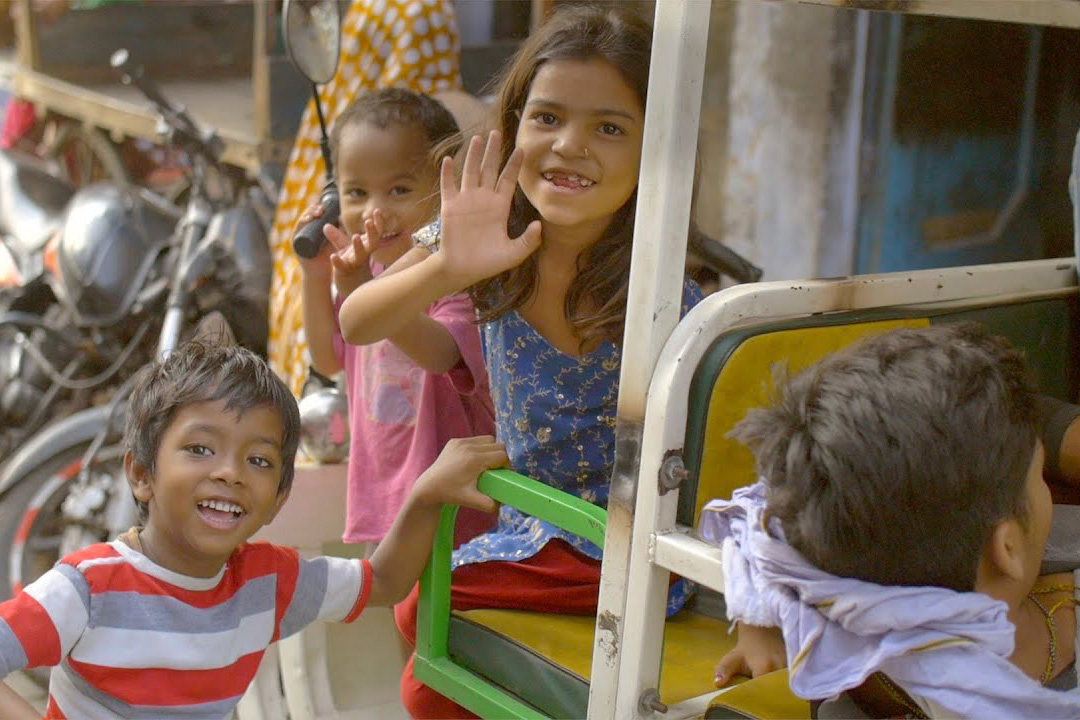 Three kids run along an auto rickshaw