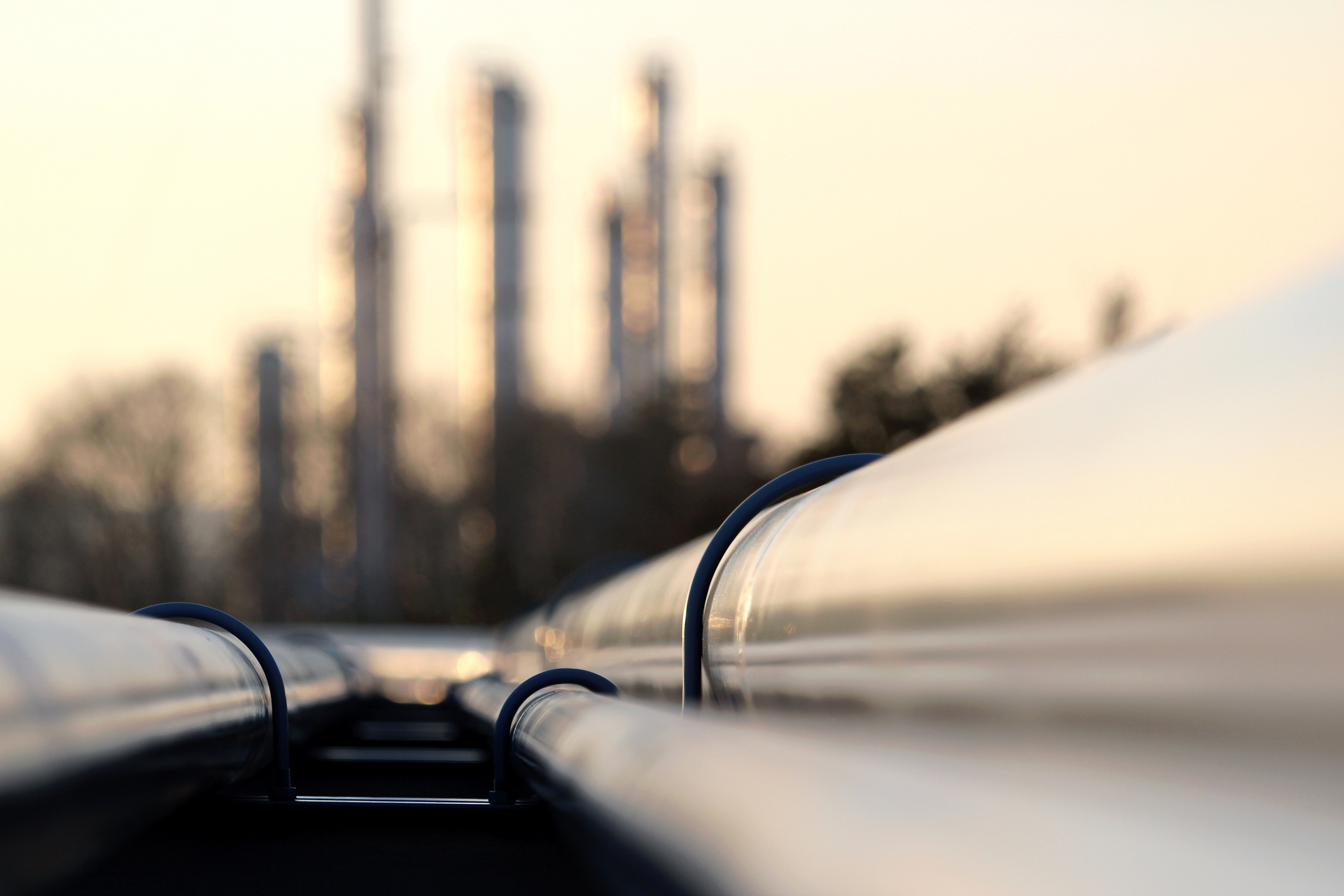 closeup of gas pipes with a refinery in the background