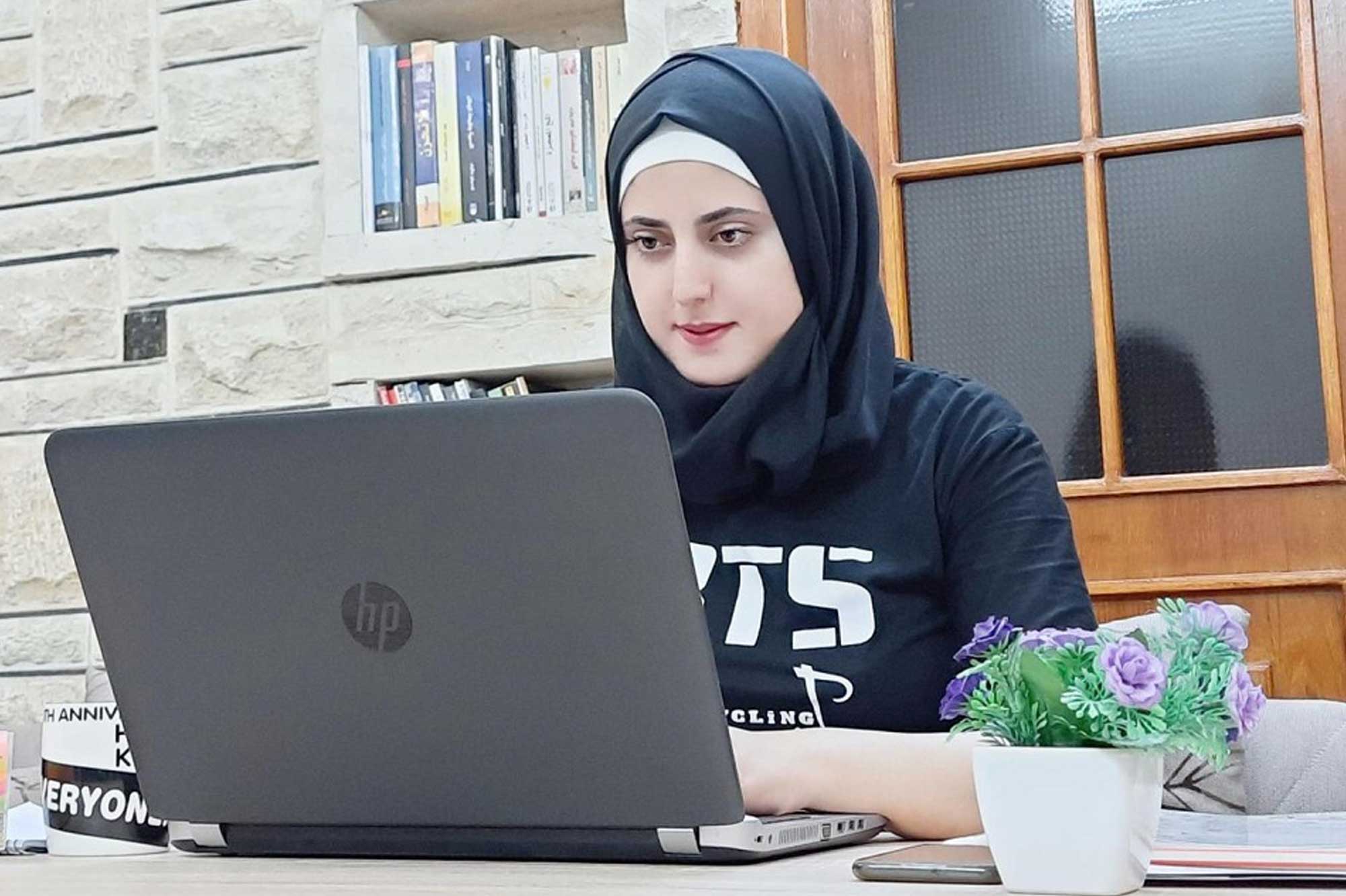 A young woman wearing a veil is working on a laptop.