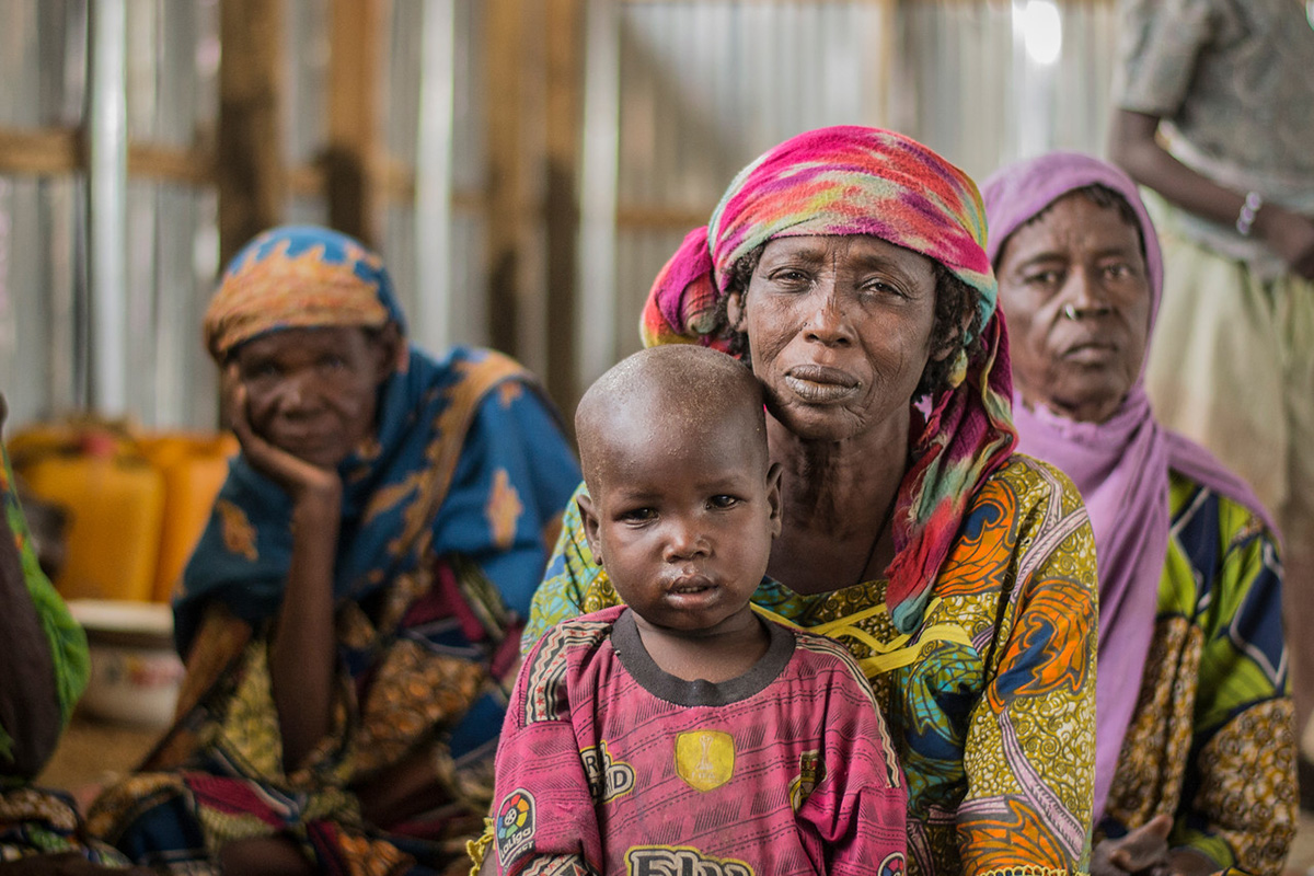 Portrait of a woman and child sitting on the ground with two other women behind.