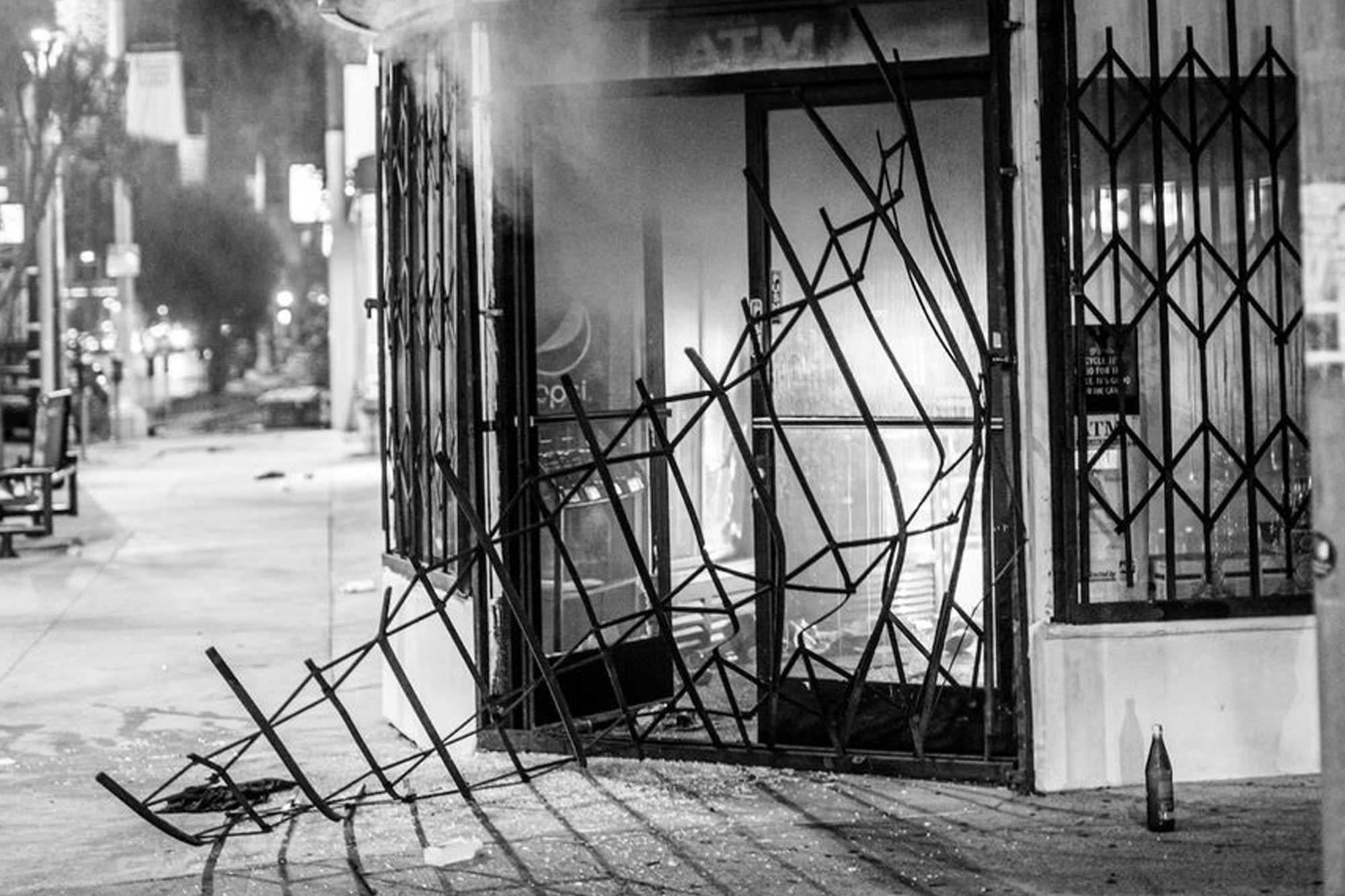 A black and white photo depicting a destroyed storefront with smoke in the background