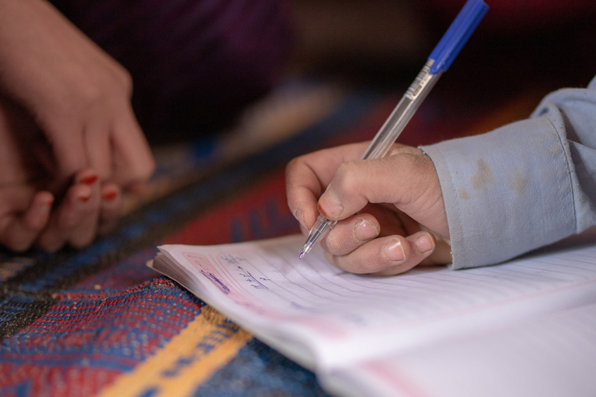 a child’s hand holding a pen writing on a notebook