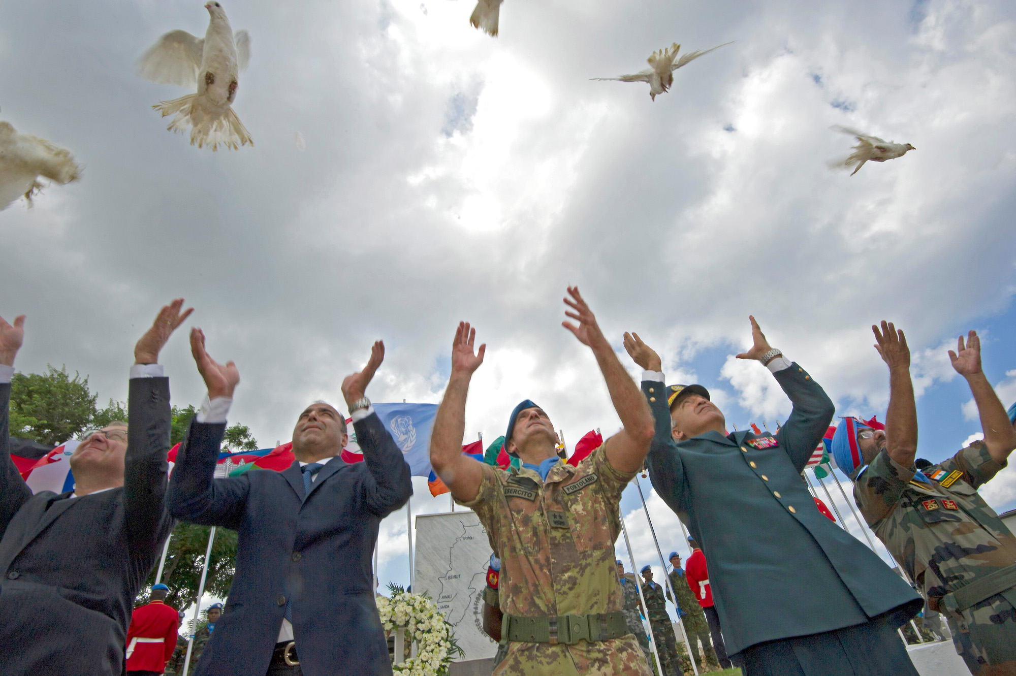 Two men in suits and two men in military officer uniforms release doves unto the air