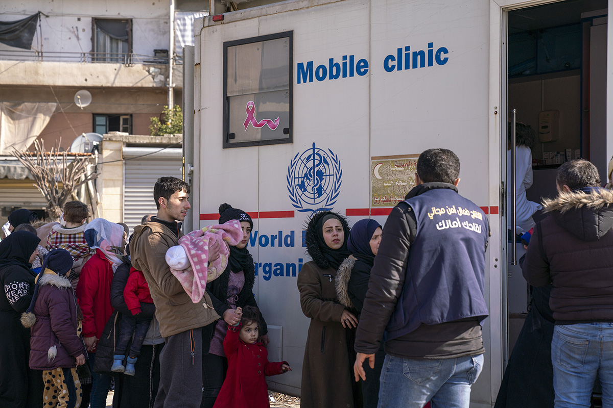 Adults and children stand in line a mobile clinic