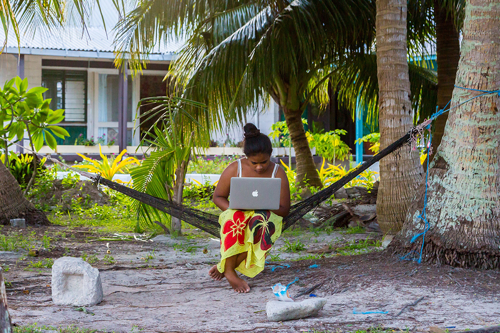 Young Polynesian woman in a hammock with a notebook working outdoors under palm trees.