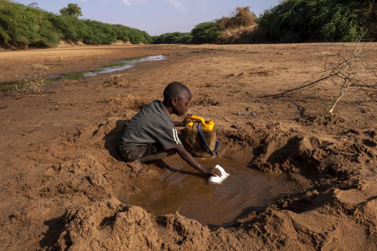 A boy gathers water from a puddle in the sand.