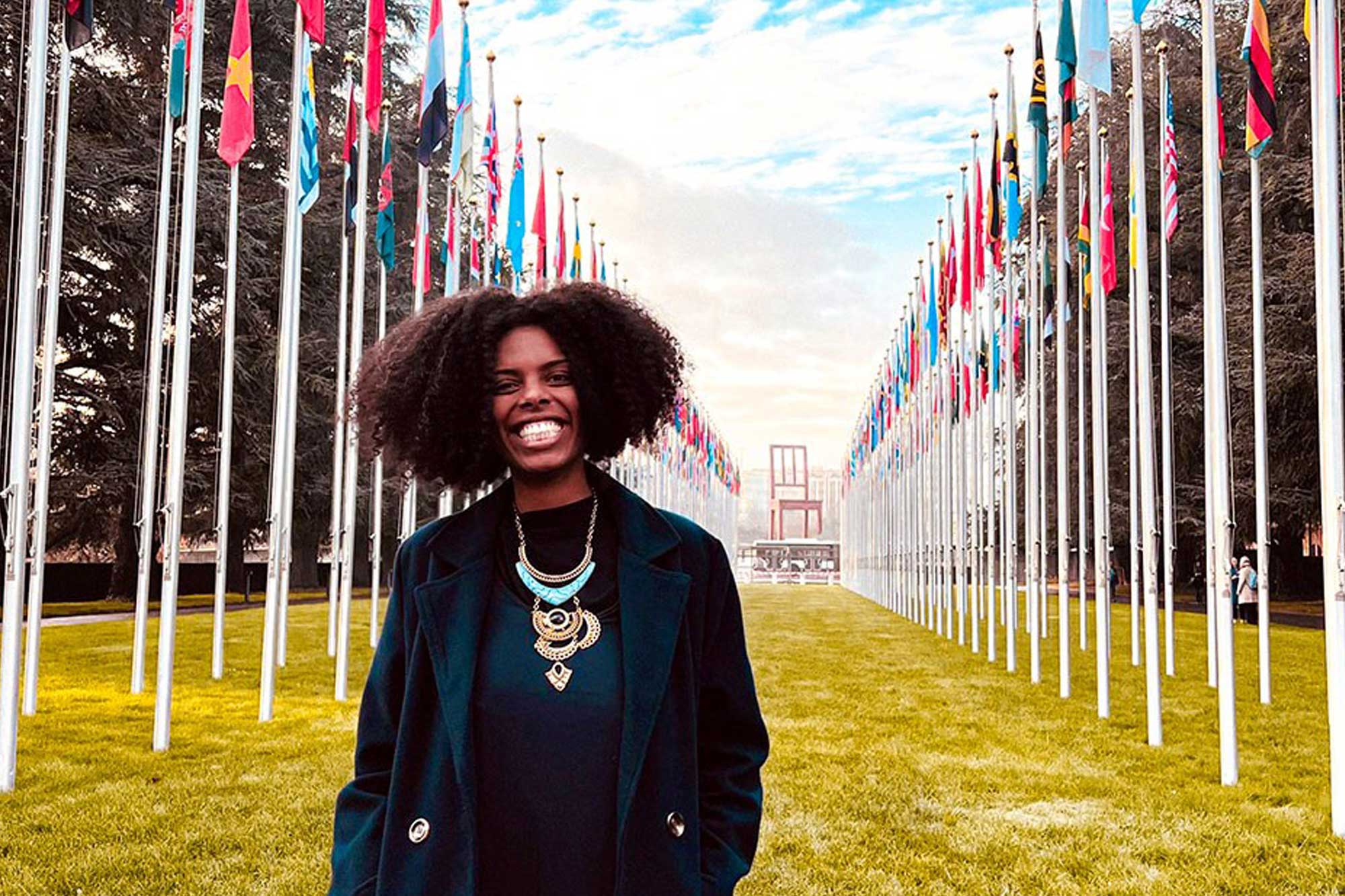 Monique stands in an open space with 2 rows of flags behind her