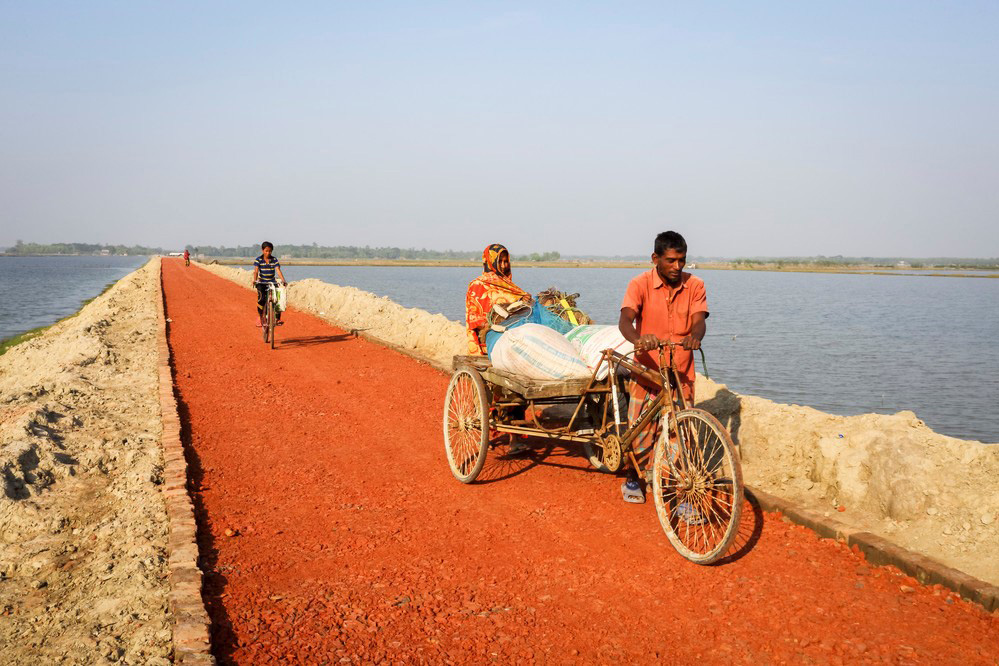 A man taking a bicycle pull cart on a new road crossing a body of water. 