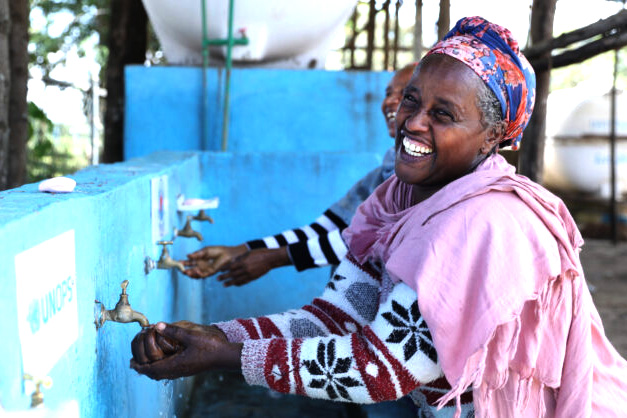 A smiling woman washes her hands.