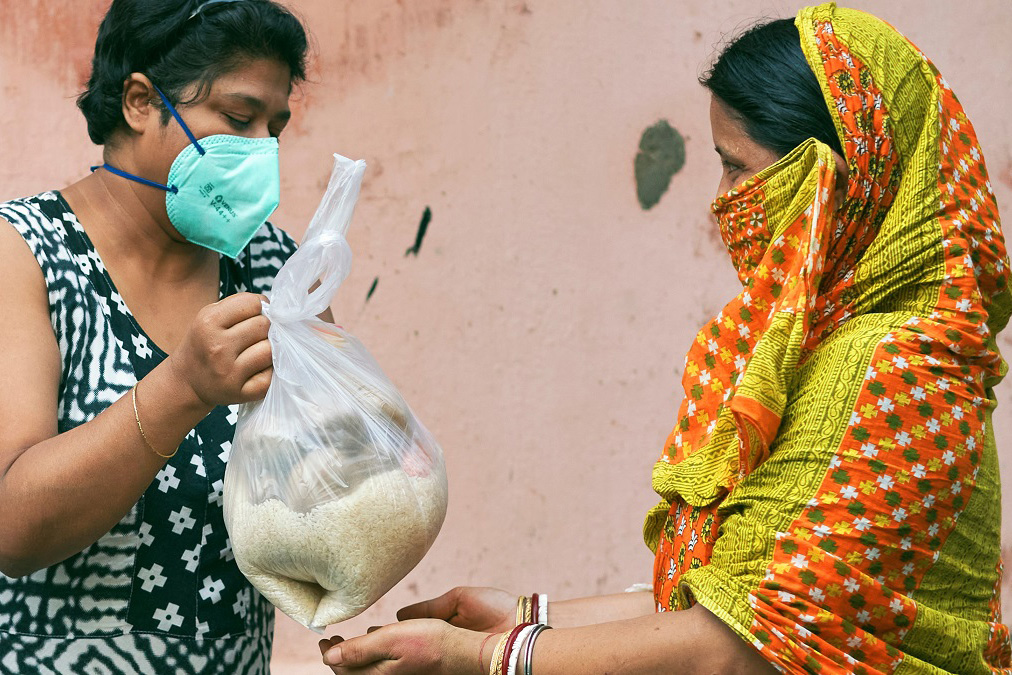 A woman hands a plastic bag full of rice and other rations to another woman. 