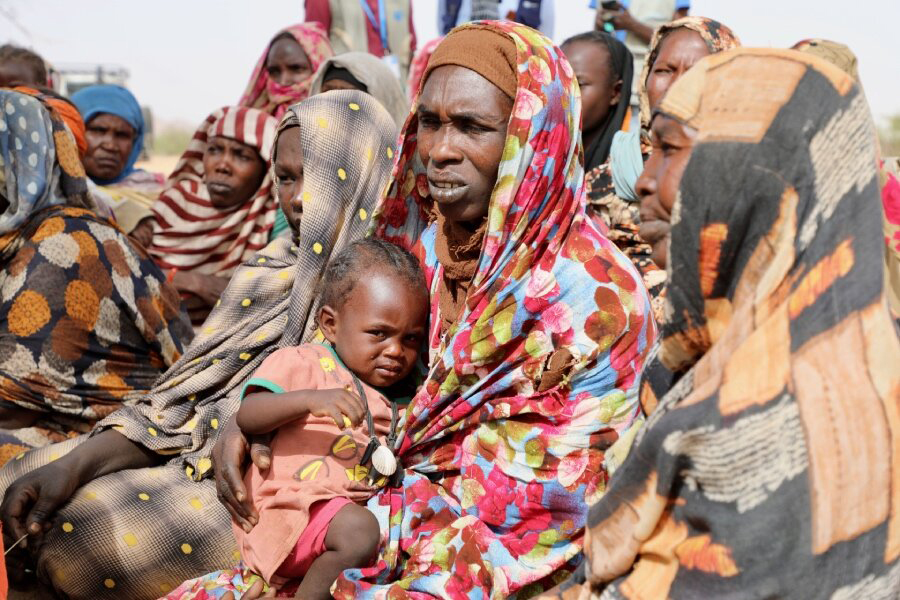 Aicha sits with her daughter on her lap among other refugees.