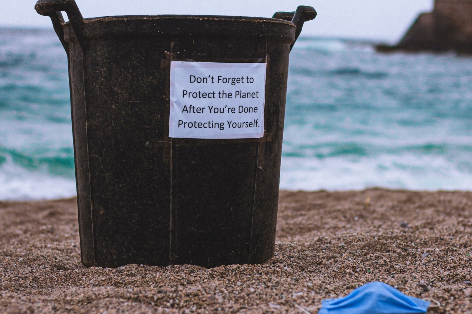 A garbage can in the beach with a sign that reads: “Don’t forget to protect the planet after you’re done protecting yourself”.