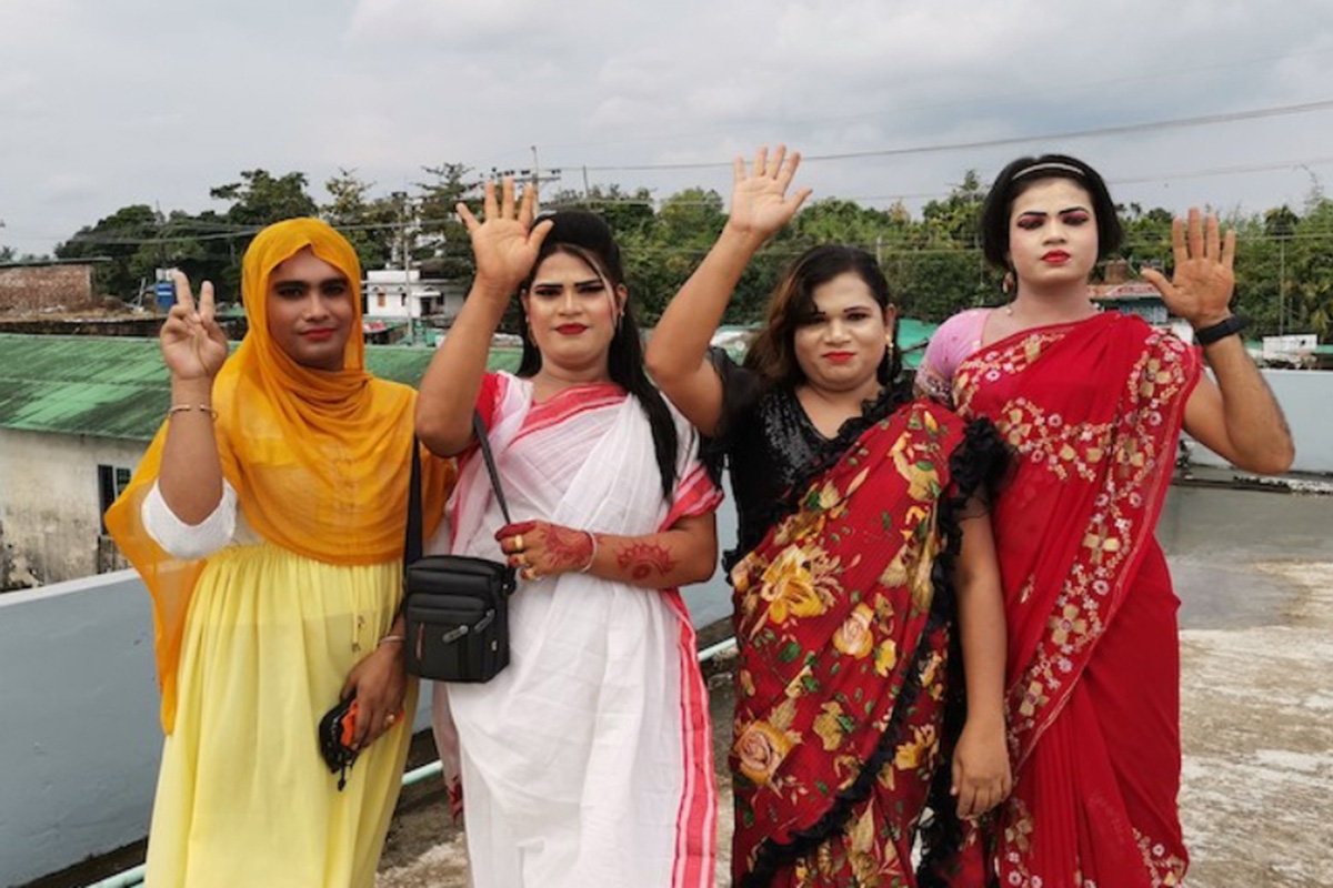 Four people representing the LGBTQIA+ community pose holding an open hand up.