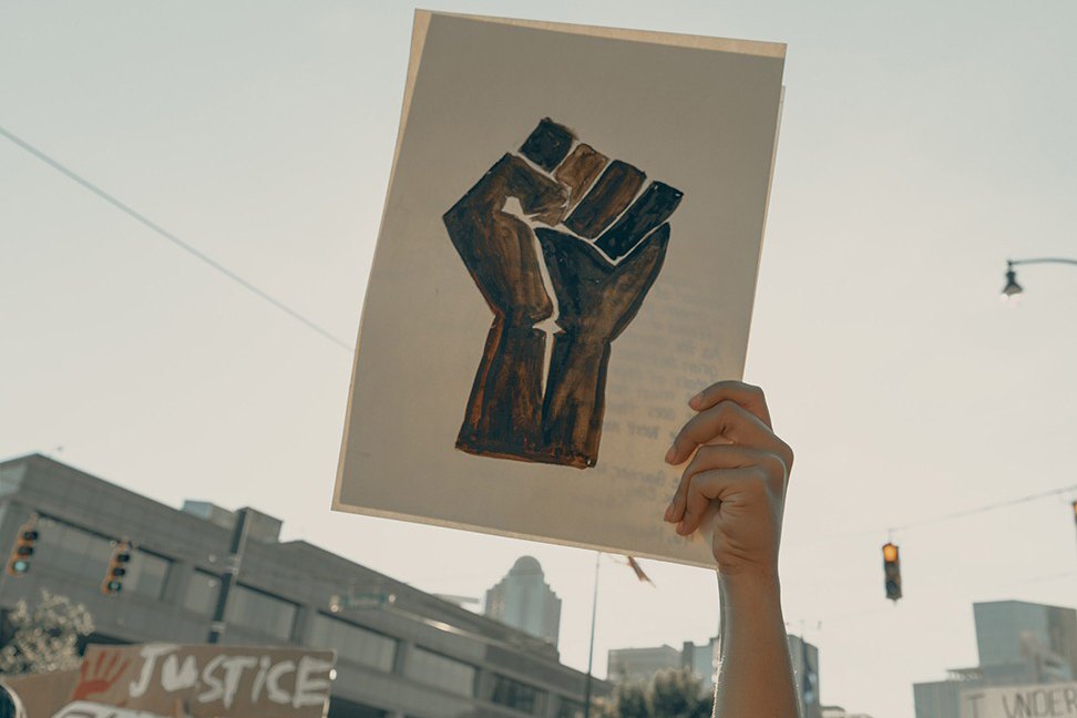 a hand holding up a protest sign portraying a fist. 