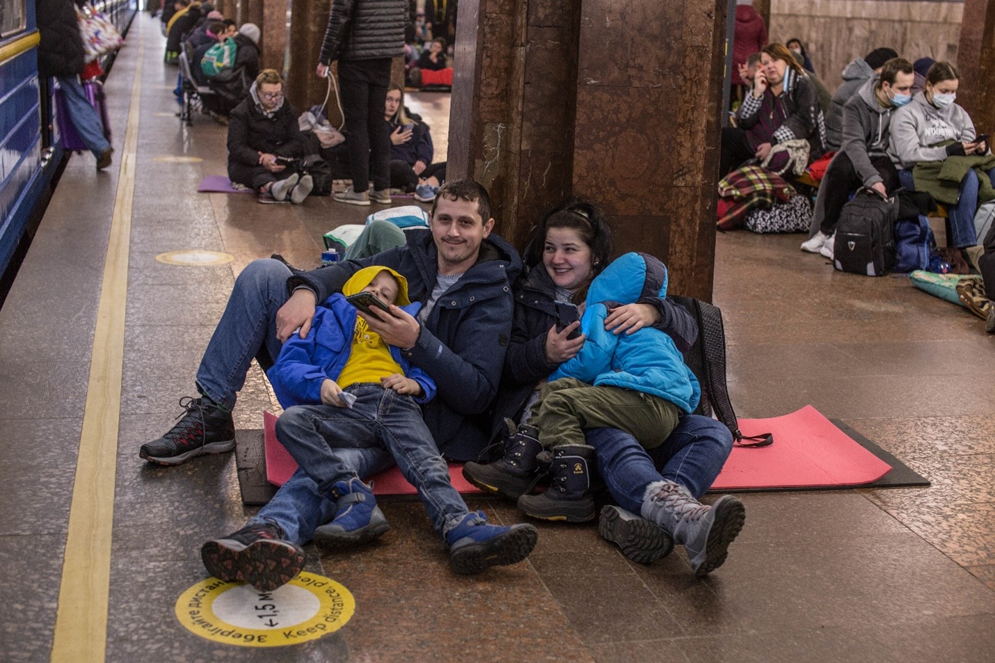 Un couple et deux enfants dans un gare, tenant des téléphones portables