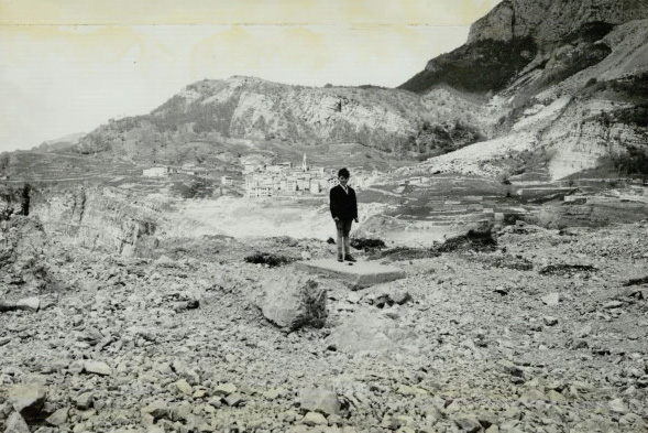 Image en noir et blanc d'un garçon debout sur un terrain rocheux avec une ville en arrière-plan.