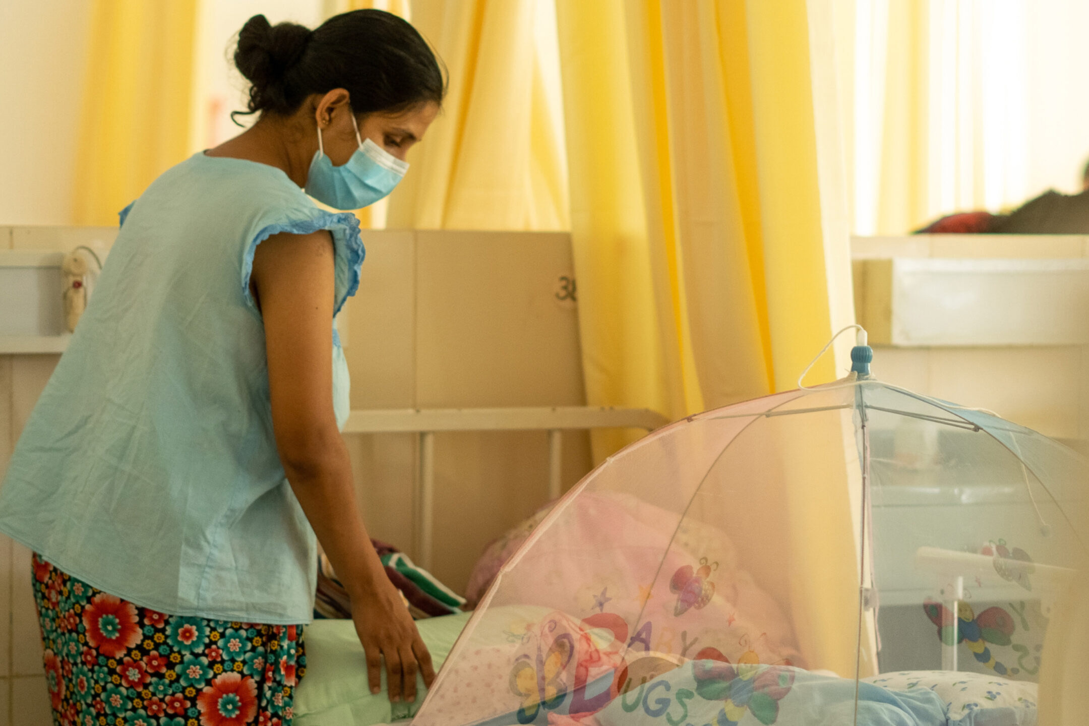 a woman looks over a baby sleeping under a net.