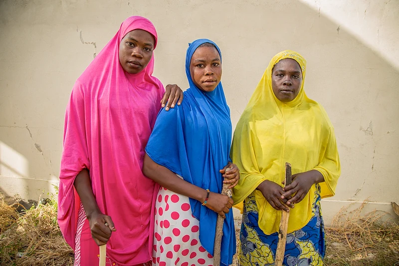 Trois femmes dans des vêtements colorés tenant des bâtons