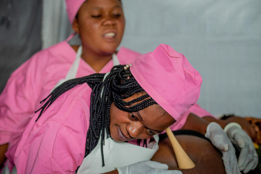 a midwife listens through a fetoscope on a woman’s belly