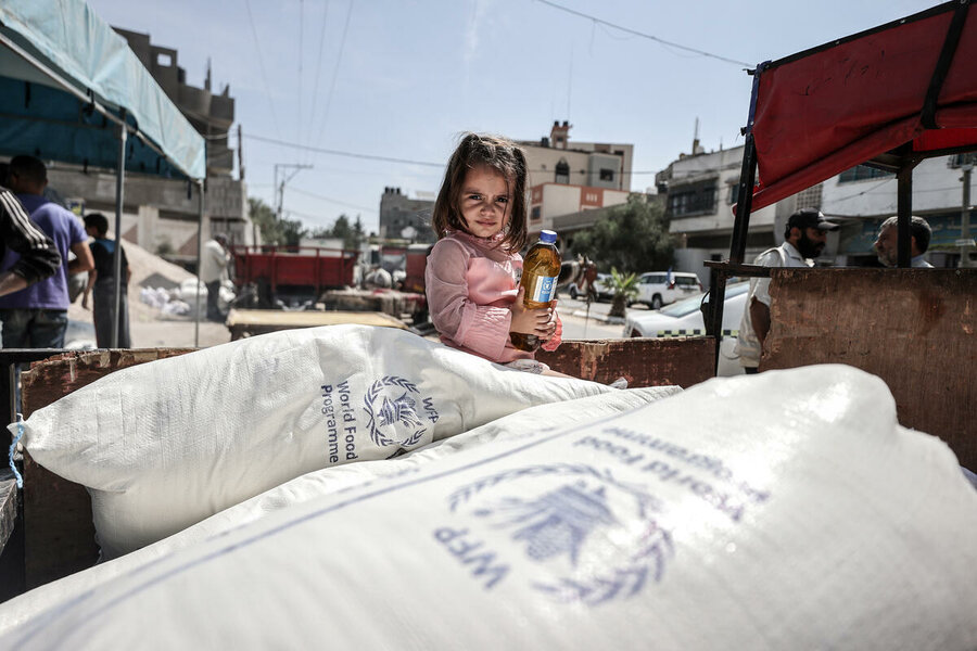a girl sits on top of a truck packed with sacks marked WFP