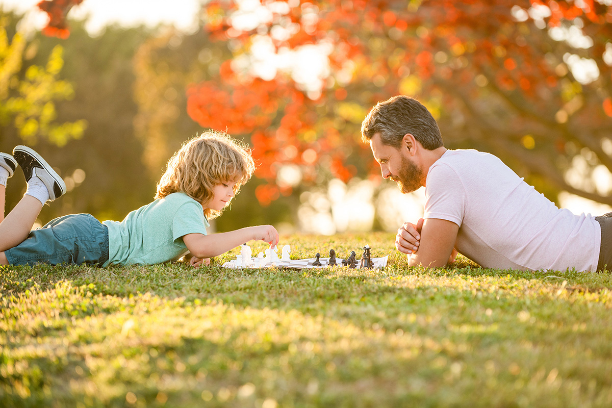 Father and son playing chess in the park.