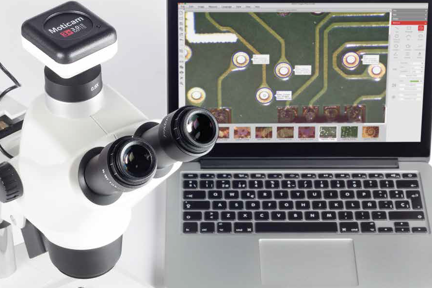 A photo of a microscope next to a laptop.