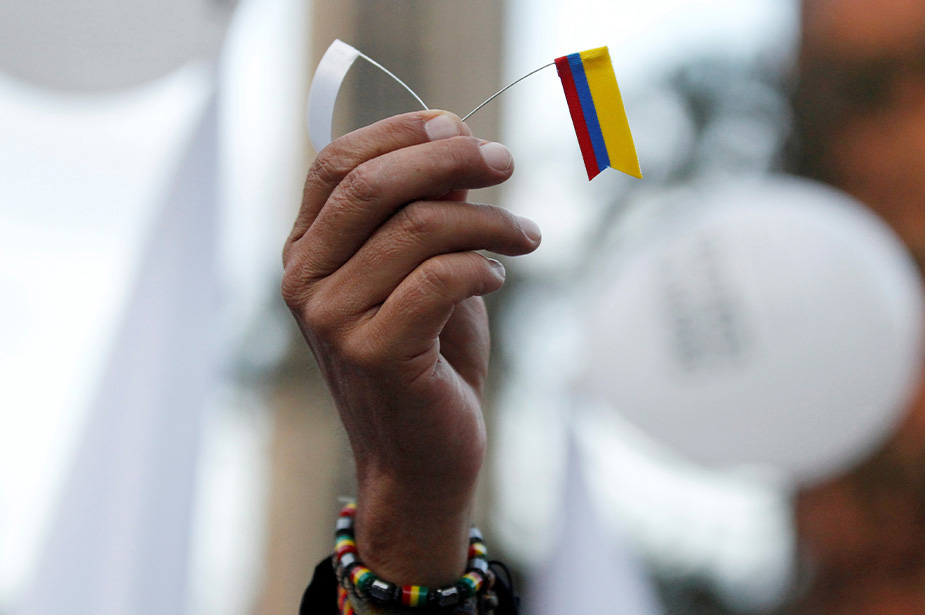 A hand holding up a white flag and Colombian flag